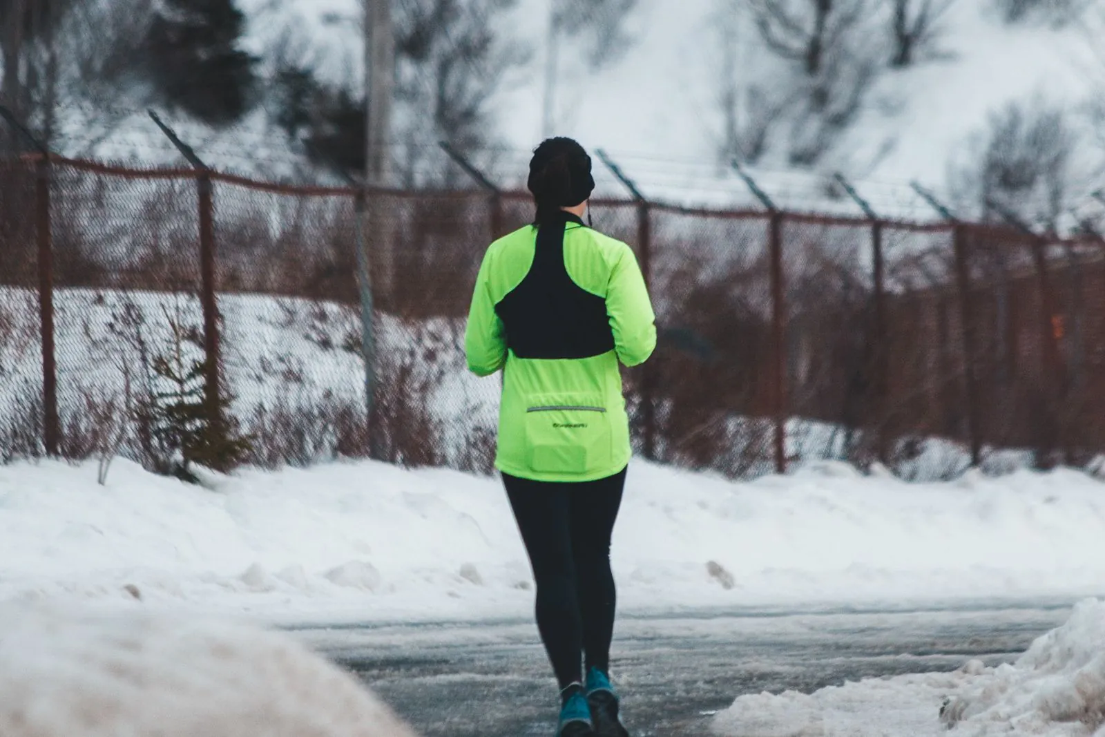 Coureur en veste fluo réfléchissante sur un chemin enneigé